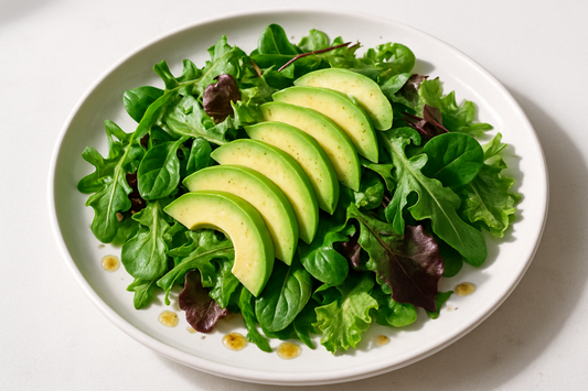 mixed salad greens with sliced avocado and drops of vinegrette visible